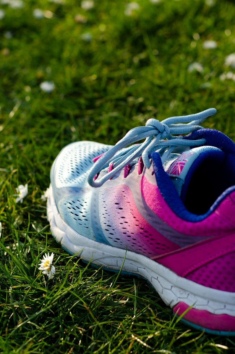 close up photo of blue and pink running shoe on green grass